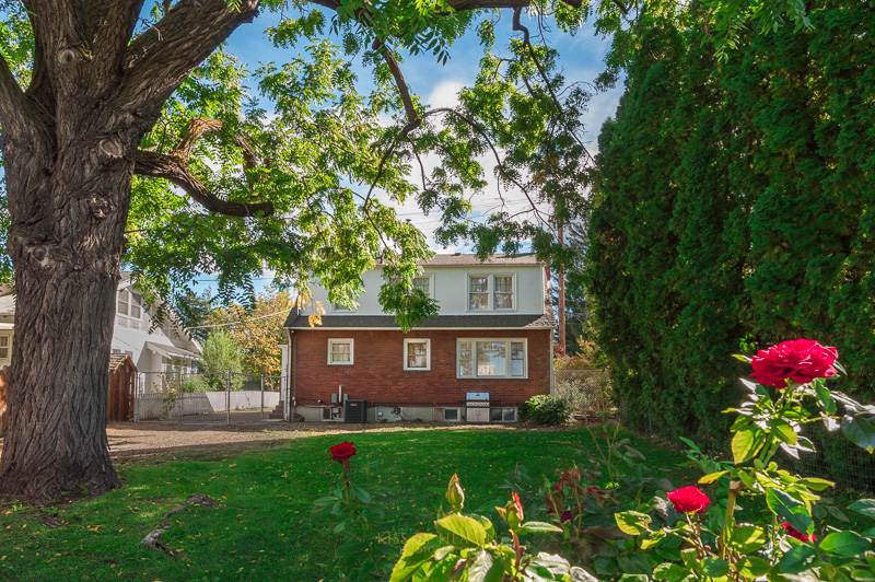 An exterior of a brick home in Yakima, WA with green yard, a big tree, and flowers. Real Estate photography service of by Kiss of Heaven Photography.