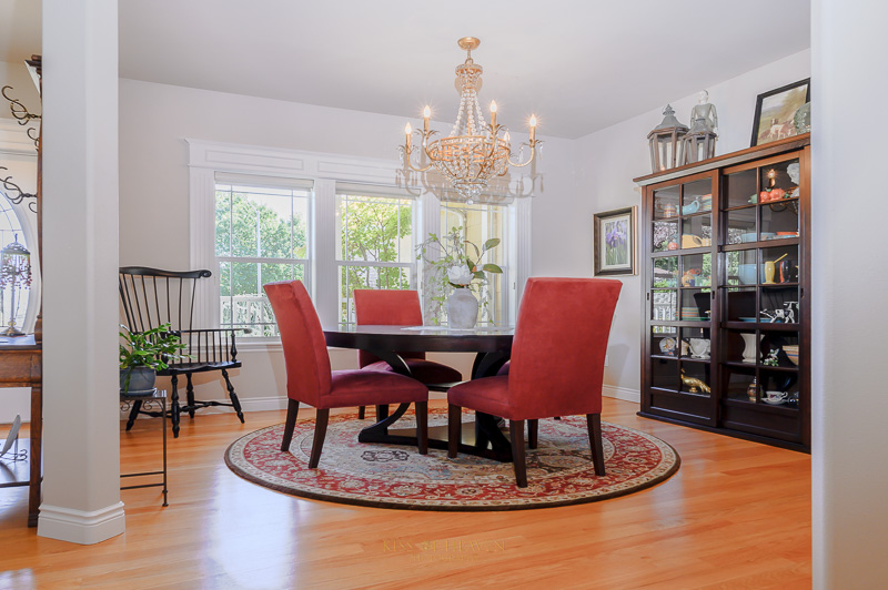 Interior of a dining room with a chandelier and red chairs and wooden floor in a luxury home. Real estate photography service by Kiss of Heaven Photography.