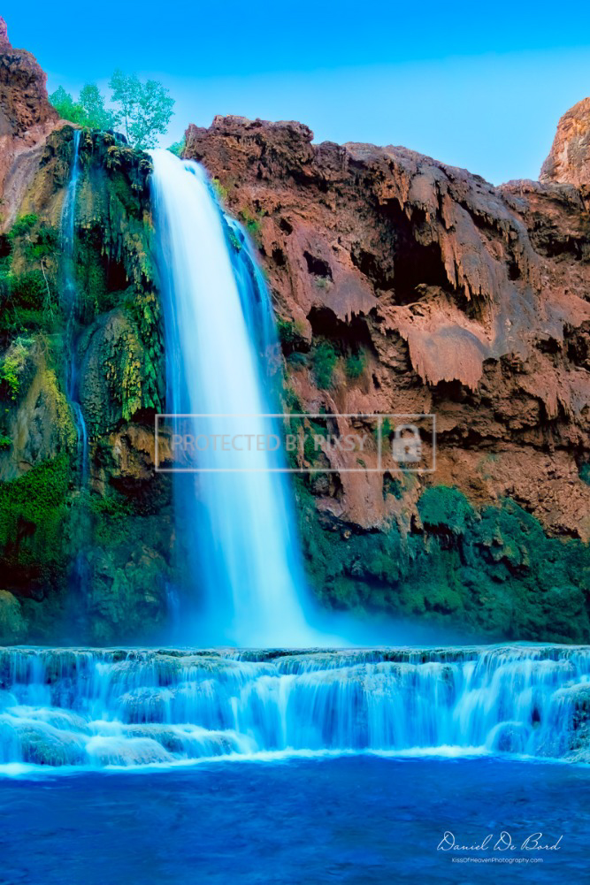 Fine art photograph of a Grand Canyon waterfall cascading into a vibrant blue pool surrounded by red rock cliffs.
